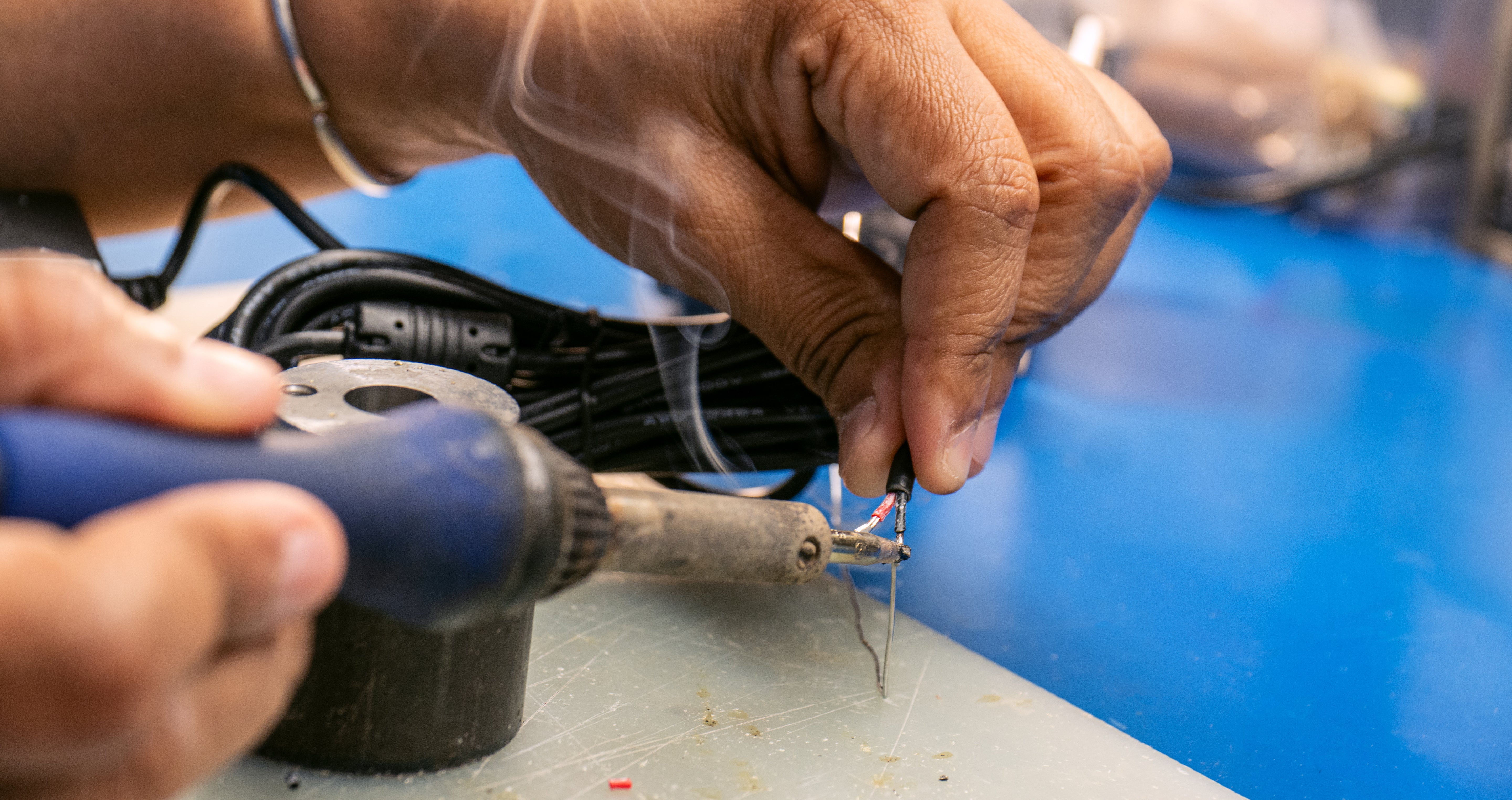 Indipro Engineer using a soldering gun on a small electronic component cable against a blue background